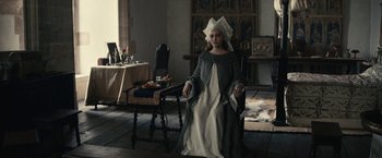 Movie still from “The King” (2019), directed by David Michôd – A woman sitting in a chair in a living room; Medium shot, Low angle