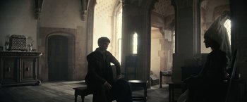 Movie still from “The King” (2019), directed by David Michôd – A man sitting on a chair in a room with tall windows; Wide shot, Low angle
