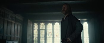 Movie still from “The King” (2019), directed by David Michôd – A man standing next to a window in a room; Medium shot, Low angle