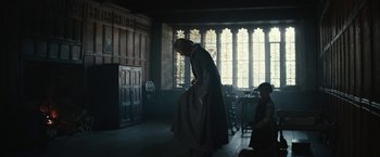 Movie still from “The King” (2019), directed by David Michôd – A woman in a long coat standing in front of a window; Wide shot, Low angle