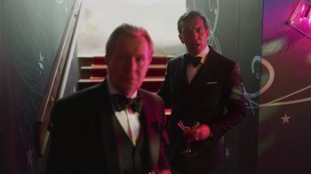 Movie still from “The Laundromat” (2019), directed by Steven Soderbergh – Two men in tuxedos standing next to each other holding drinks; Medium shot, Over the shoulder angle