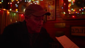 Movie still from “The Laundromat” (2019), directed by Steven Soderbergh – An older man sitting at a table with a glass of wine; Close Up shot, Over the shoulder angle