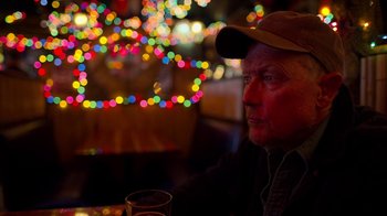 Movie still from “The Laundromat” (2019), directed by Steven Soderbergh – An older man sitting at a table with a glass of wine; Close Up shot, Over the shoulder angle