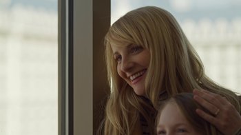 Movie still from “The Laundromat” (2019), directed by Steven Soderbergh – A woman with long blonde hair smiles at the camera while a child looks on; Close Up shot, Low angle
