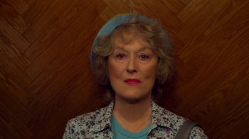 Movie still from “The Laundromat” (2019), directed by Steven Soderbergh – An older woman wearing a blue hat and a blue shirt; Close Up shot, Overhead angle