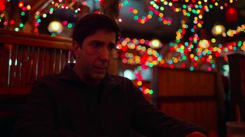 Movie still from “The Laundromat” (2019), directed by Steven Soderbergh – A man sitting in front of christmas lights in a room; Close Up shot, Low angle