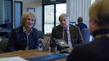Movie still from “The Laundromat” (2019), directed by Steven Soderbergh – A man and a woman sitting in front of a computer; Medium shot, Over the shoulder angle