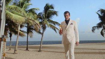 Movie still from “The Laundromat” (2019), directed by Steven Soderbergh – A man in a white suit holding a bottle of alcohol; Wide shot, Low angle