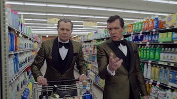 Movie still from “The Laundromat” (2019), directed by Steven Soderbergh – A couple of men standing next to each other in a store; Medium shot, Low angle