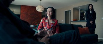 Movie still from “The Laundromat” (2019), directed by Steven Soderbergh – A woman sitting on a couch holding a wine glass; Medium shot, Over the shoulder angle