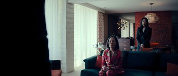 Movie still from “The Laundromat” (2019), directed by Steven Soderbergh – A woman sitting on top of a couch in a living room; Medium shot, High angle