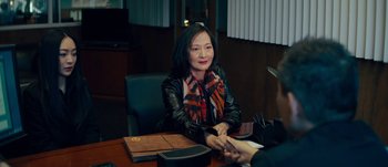 Movie still from “The Laundromat” (2019), directed by Steven Soderbergh – A woman sitting at a table with a book; Medium shot, Over the shoulder angle