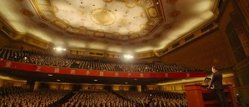 Movie still from “The Laundromat” (2019), directed by Steven Soderbergh – A large crowd of people are in a large auditorium; Extreme Wide shot, High angle