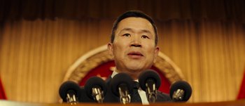 Movie still from “The Laundromat” (2019), directed by Steven Soderbergh – A person at a podium with microphones; Close Up shot, Low angle