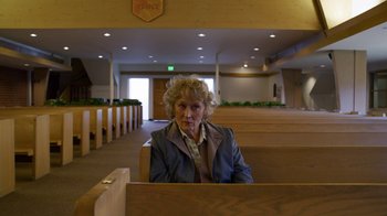 Movie still from “The Laundromat” (2019), directed by Steven Soderbergh – An older woman sitting in a pew in a church; Medium shot, High angle