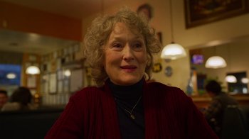 Movie still from “The Laundromat” (2019), directed by Steven Soderbergh – An older woman wearing a black shirt and a red sweater; Close Up shot, Over the shoulder angle