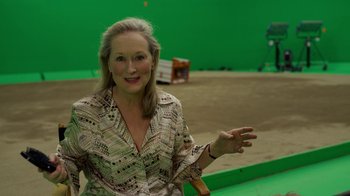 Movie still from “The Laundromat” (2019), directed by Steven Soderbergh – A woman is smiling and holding her hand out; Medium shot, High angle