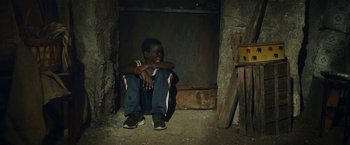 Movie still from “The Life Ahead” (2020), directed by Edoardo Ponti – A man sitting on the ground with his arms crossed; Wide shot, High angle