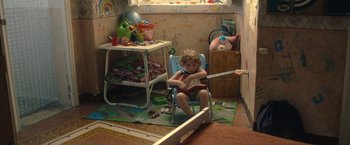 Movie still from “The Life Ahead” (2020), directed by Edoardo Ponti – A little boy sitting in a chair holding a guitar; Medium shot, High angle