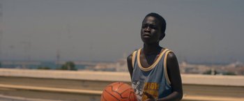 Movie still from “The Life Ahead” (2020), directed by Edoardo Ponti – A young man holding a basketball in his hands; Medium shot, Low angle