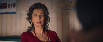 Movie still from “The Life Ahead” (2020), directed by Edoardo Ponti – An older woman wearing a red shirt and a red necklace; Close Up shot, Over the shoulder angle