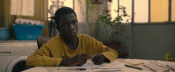 Movie still from “The Life Ahead” (2020), directed by Edoardo Ponti – A young man sitting at a table in front of papers; Close Up shot, Over the shoulder angle