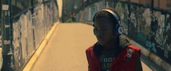 Movie still from “The Life Ahead” (2020), directed by Edoardo Ponti – A young man wearing headphones while standing on the side of a road; Close Up shot, Low angle