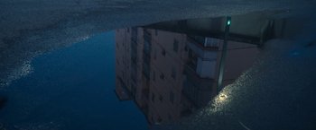 Movie still from “The Life Ahead” (2020), directed by Edoardo Ponti – A building reflected in a puddle of water at night; Extreme Wide shot, High angle