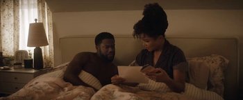 Movie still from “The Man from Toronto” (2022), directed by Patrick Hughes – A man and a woman in a bed reading a paper; Medium shot, High angle