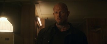 Movie still from “The Man from Toronto” (2022), directed by Patrick Hughes – A man with a beard and a black shirt is standing in a room; Close Up shot, Over the shoulder angle