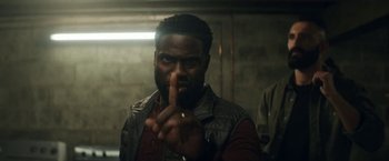Movie still from “The Man from Toronto” (2022), directed by Patrick Hughes – A man making a peace sign with his hand; Close Up shot, Over the shoulder angle