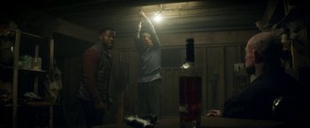 Movie still from “The Man from Toronto” (2022), directed by Patrick Hughes – Two men standing next to each other in a dark room; Medium shot, Over the shoulder angle