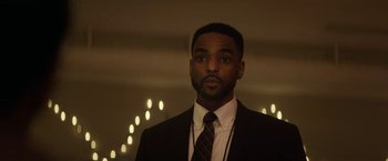 Movie still from “The Man from Toronto” (2022), directed by Patrick Hughes – A man wearing a suit and tie standing in front of candles; Close Up shot, Low angle
