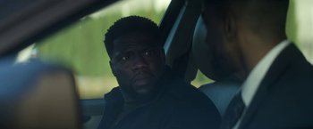 Movie still from “The Man from Toronto” (2022), directed by Patrick Hughes – A person sitting in a car; Close Up shot, Over the shoulder angle