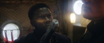 Movie still from “The Man from Toronto” (2022), directed by Patrick Hughes – A person holding a gun in a room; Close Up shot, Low angle