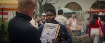 Movie still from “The Man from Toronto” (2022), directed by Patrick Hughes – A man holding a box with a shirt on it; Medium shot, Over the shoulder angle