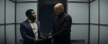 Movie still from “The Man from Toronto” (2022), directed by Patrick Hughes – Two men standing next to each other in front of an elevator; Medium shot, Over the shoulder angle