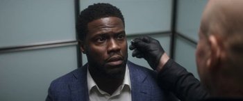 Movie still from “The Man from Toronto” (2022), directed by Patrick Hughes – A person wearing a suit and a glove; Close Up shot, Over the shoulder angle