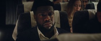 Movie still from “The Man from Toronto” (2022), directed by Patrick Hughes – A person sitting in a chair on a train; Close Up shot, Over the shoulder angle