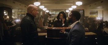 Movie still from “The Man from Toronto” (2022), directed by Patrick Hughes – Two men and a woman standing in front of a counter; Medium shot, Over the shoulder angle