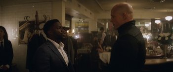 Movie still from “The Man from Toronto” (2022), directed by Patrick Hughes – Two men in suits are talking to each other in a restaurant; Medium shot, Over the shoulder angle