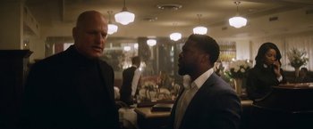 Movie still from “The Man from Toronto” (2022), directed by Patrick Hughes – Two men in suits are talking in a restaurant; Medium shot, Over the shoulder angle