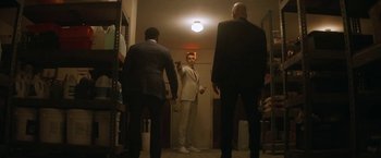 Movie still from “The Man from Toronto” (2022), directed by Patrick Hughes – A man in a suit and tie standing in front of two other men; Wide shot, Low angle