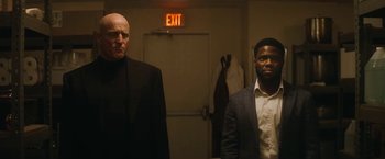 Two men standing in front of an exit sign in a darkened room