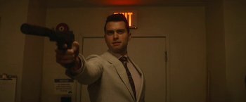 Movie still from “The Man from Toronto” (2022), directed by Patrick Hughes – A man wearing a suit and tie holding a gun; Close Up shot, Over the shoulder angle