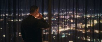 Movie still from “The Man from Toronto” (2022), directed by Patrick Hughes – A man standing in front of a window at night; Wide shot, Over the shoulder angle