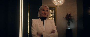Movie still from “The Man from Toronto” (2022), directed by Patrick Hughes – A woman in a white suit posing for a picture; Medium shot, Over the shoulder angle