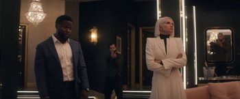 Movie still from “The Man from Toronto” (2022), directed by Patrick Hughes – A man and a woman standing in front of another man in a suit; Medium shot, Over the shoulder angle