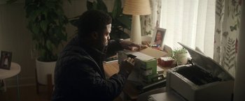 Movie still from “The Man from Toronto” (2022), directed by Patrick Hughes – A man sitting at a table looking at a box; Medium shot, High angle