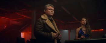 Movie still from “The Man from Toronto” (2022), directed by Patrick Hughes – A man in a brown jacket standing in front of a building; Medium shot, Low angle